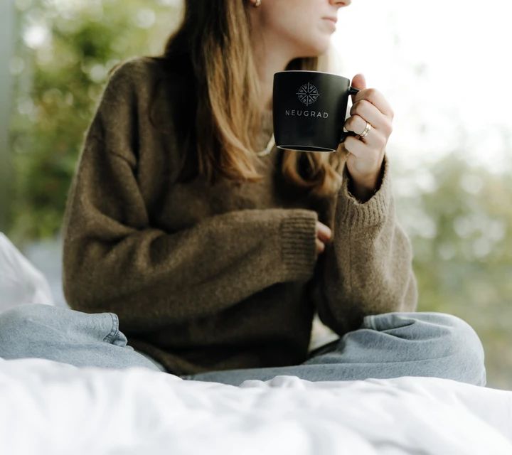 Frau trinkt Kaffee aus einer mit Neugrad Logo bedruckten Tasse